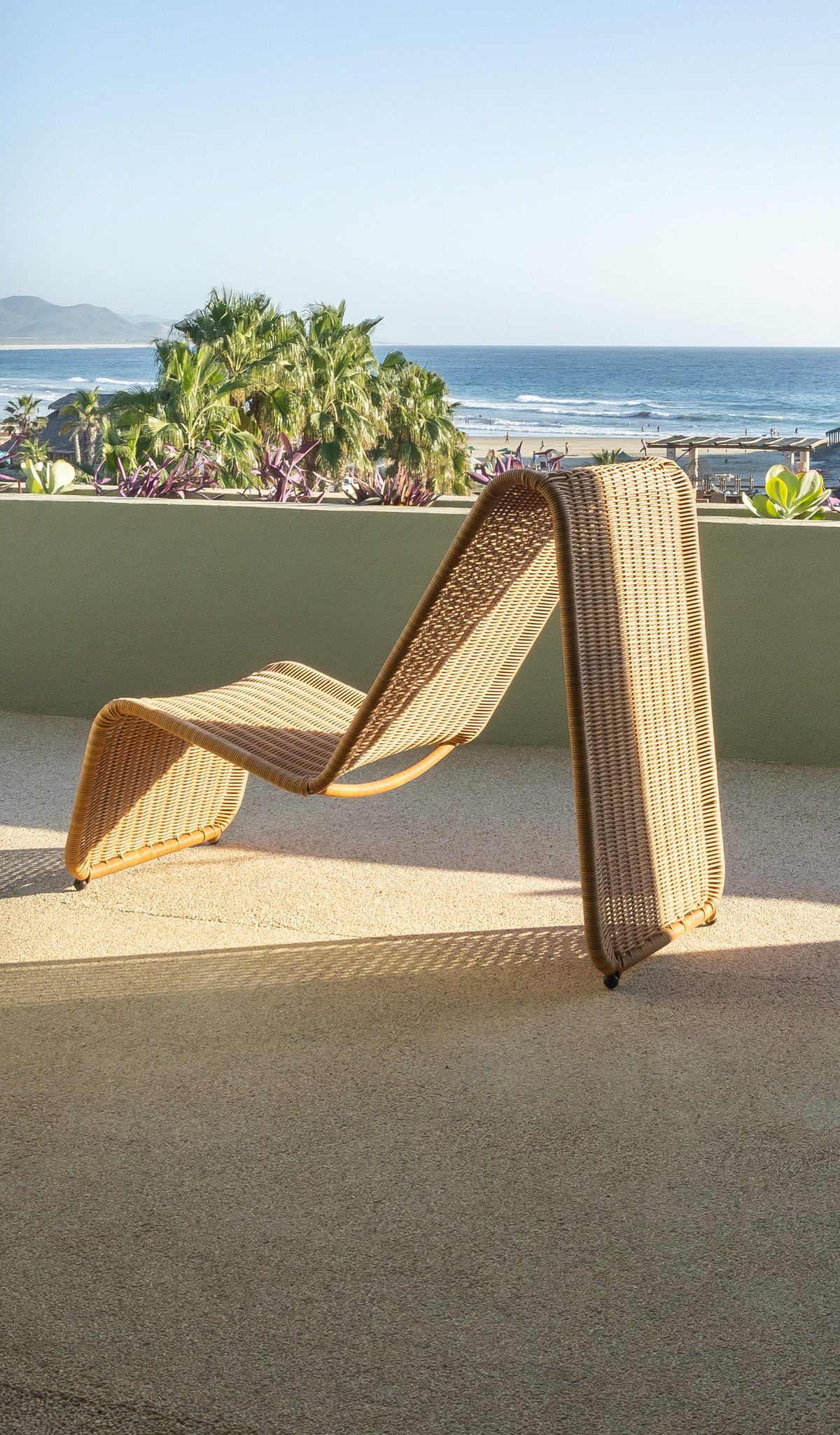 A wicker lounge chair on the penthouse balcony, seen through the doorway, with the beach and the Pacific beyond